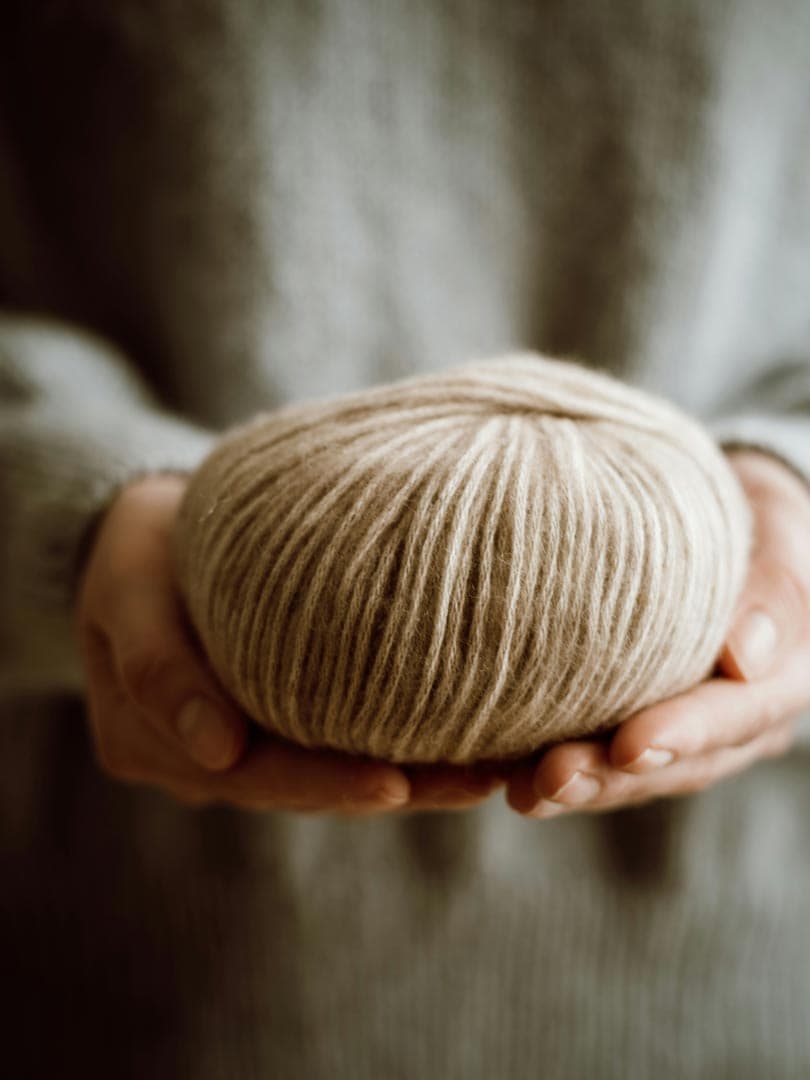 Two hands cradling a ball of undyed cream wool
